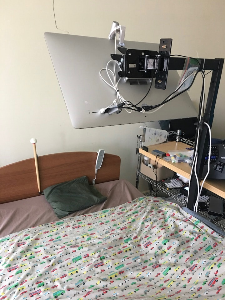 The finished mount beside a bed, with a monitor held on a bracket at the top of a tall pole over the bed