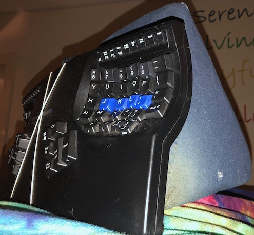 A compact ergonomic keyboard mounted on an angled foam wedge, photographed against a brightly patterned blanket